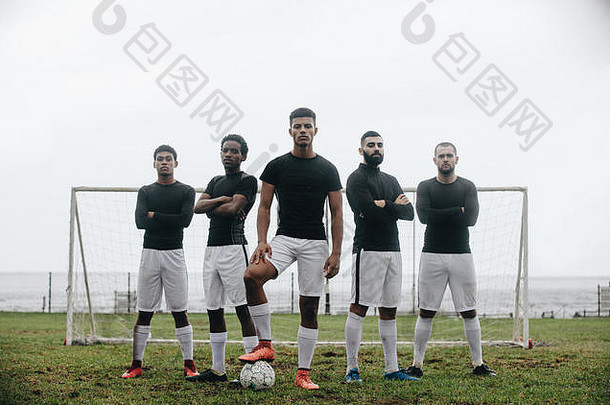五名<strong>足球</strong>运动员站在门柱前形成队形。<strong>足球</strong>运动员单脚站在球上，队友站在他身后