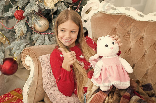 小孩子快乐微笑现在女孩可爱的兔子圣诞节树小女孩持有兔子<strong>玩具</strong>孩子显示拇指软<strong>玩具</strong>圣诞节<strong>玩具</strong>
