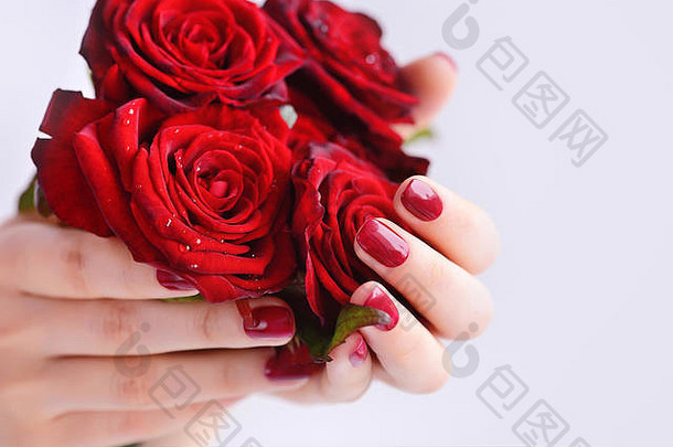 一位修了深红色指甲，手上插着一束红玫瑰的女士