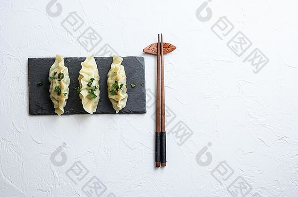 泡菜饺子肉饺子在白色纹理背景上的黑色石头板上俯视文本空间。
