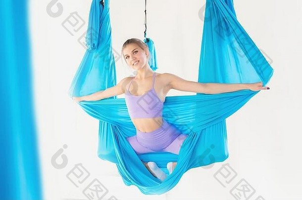 Aero fly瑜伽穿着制服的美女教练在白色课堂上展示了在蓝色吊床上伸展的体式
