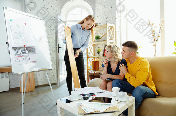 室内设计师与年轻夫妇合作。可爱的家庭和专业设计师或建筑师，讨论未来室内的概念，在现代办公室调色板和房间图纸。
