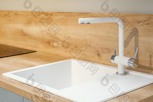 现代白色方形水槽，带长水龙头，位于光滑的木制厨房台面上，特写