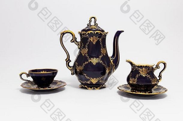 一套美丽的钴蓝色复古瓷<strong>茶具</strong>的特写镜头，白色背景上有金色<strong>花</strong>朵图案。这套包括一个茶壶，一个茶壶