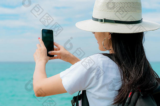 年轻的亚洲背包女游客戴着帽子在码头用智能手机自拍。在热带天堂海滩度假。快乐的时髦女孩在h上旅行
