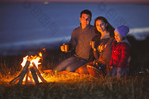 夜晚，幸福的一家人坐在秋天海滩的火堆旁