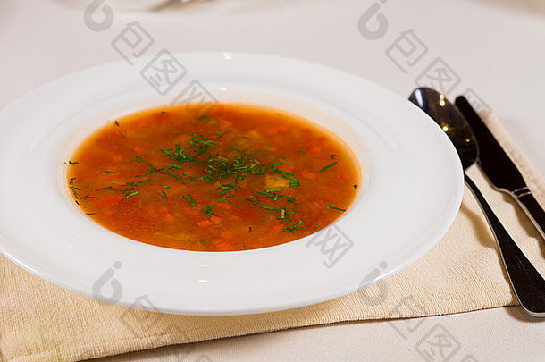 一盘营养丰富的蔬菜汤或汤，用切碎的新鲜香草装饰，放在一个白碗里，作为开胃菜