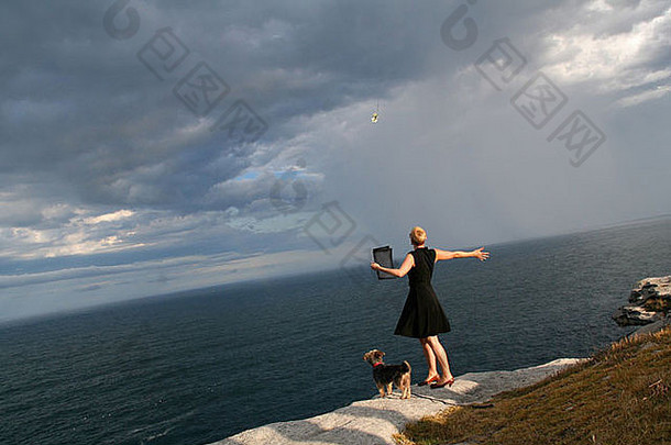 在悉尼北邦迪的悬崖上，一名妇女将一朵玫瑰花扔向大海，她的狗在观看仪式