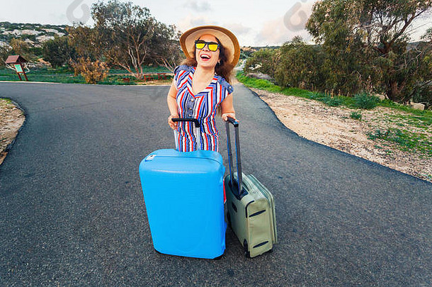 旅游、度假、暑期和度假理念——年轻女子提着手提箱站在路上大笑