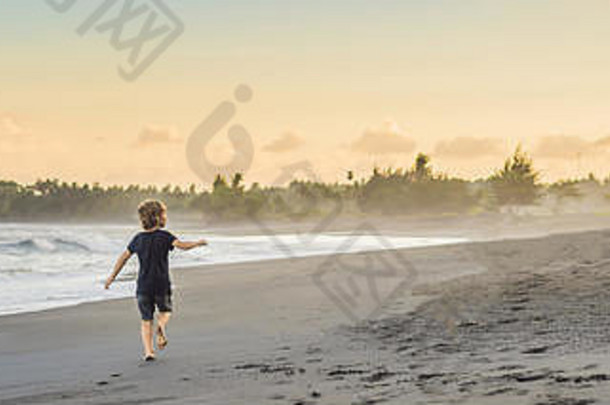 快乐的小男孩在日落旗帜下的海滩上放风筝，长格式