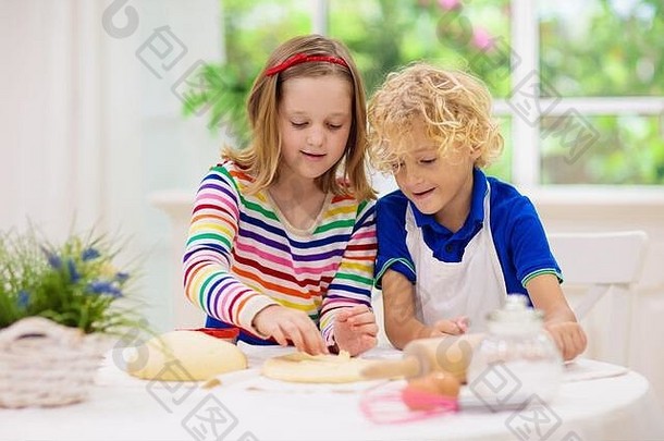 孩子们在阳光明媚的白色厨房里烤馅饼。孩子们做饭。男孩和女孩在大窗户前擀面团。儿童健康营养。兄妹
