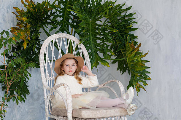 戴着大帽子的漂亮小女孩坐在一把白色的椅子上
