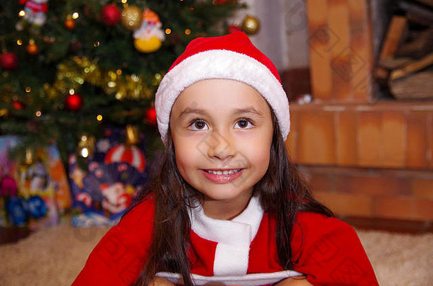 美丽的微笑着的小女孩穿着圣诞服装，背景是圣诞树和一些礼物