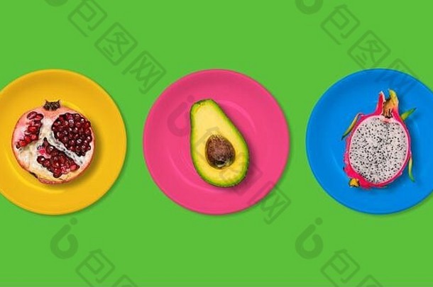 鳄梨、红石榴和火龙果放在<strong>绿色</strong>背景的彩色盘子里。素食的概念。时尚创意与夏季风格