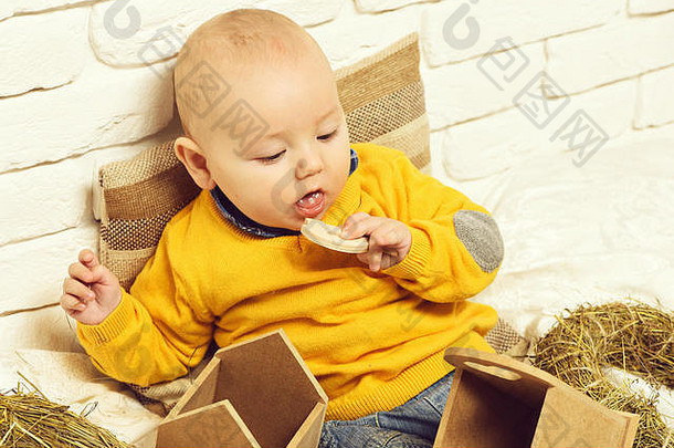 小婴儿男孩可爱的好奇的脸黄色的毛衣靠枕头玩木盒子白色砖墙背景