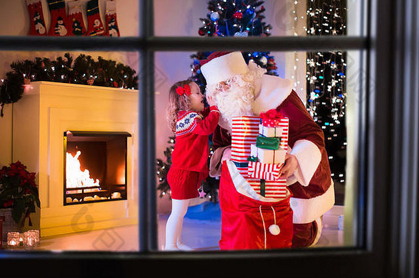 圣诞前夜，孩子们和圣诞老人在壁炉旁。家人庆祝圣诞节。用树、礼物装饰客厅