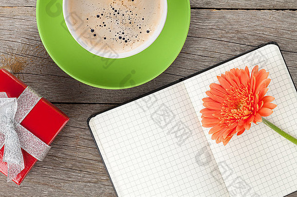 空白记事本、礼品盒、咖啡杯和木制桌子背景上的橙色非洲菊花