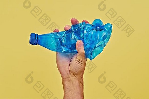 用手挤压黄色背景上的蓝色塑料瓶。零浪费和减少塑料消耗的概念。最小空间