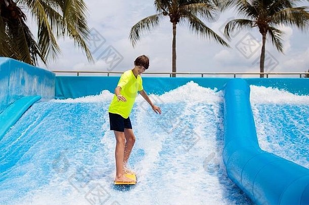 青少年在热带度假区水上游乐场的海滩波浪模拟景点冲浪。十几岁的男孩试图骑身体板。冲浪乐趣。杨
