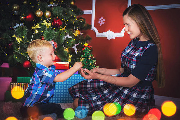 年轻的母亲和她的儿子在装饰好的房间里的圣诞树旁放着礼物。