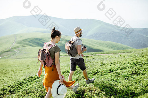 这对美丽的夫妇背着背包在绿色的草地上散步，在夏天的时候在山里旅行，玩得很开心