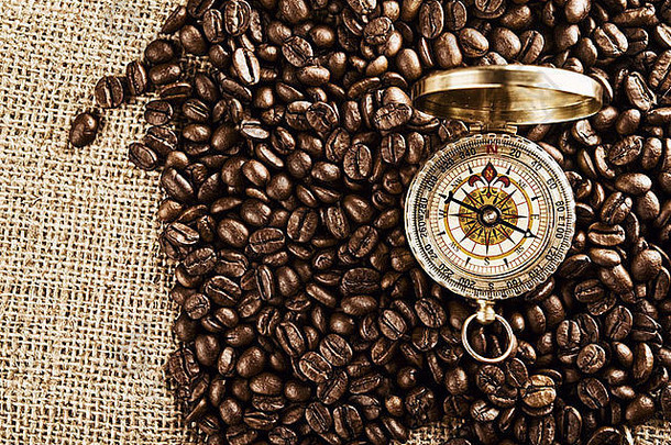 咖啡豆和指南针在黄麻帆布纹理上。