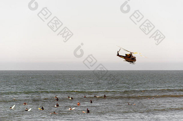 加利福尼亚州夏季，一架飞行的消防直升机在马里布海滩上空和冲浪者的视野