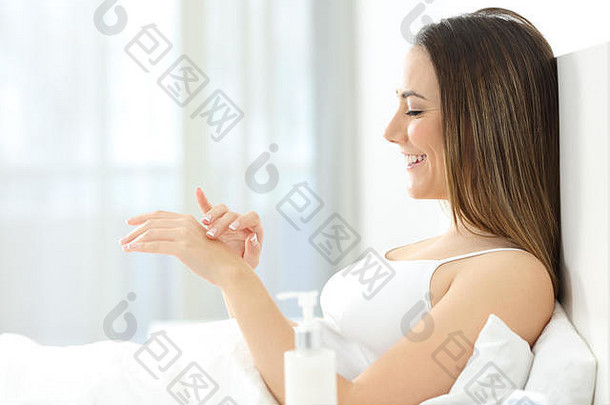 一位快乐的女士在床上双手涂抹保湿霜的侧视图
