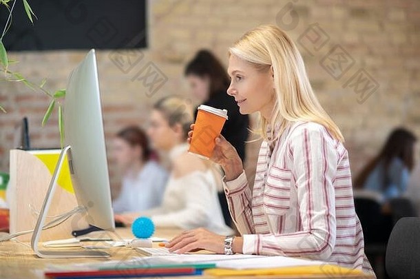 一个金发碧眼的女人在电脑前工作，喝着咖啡