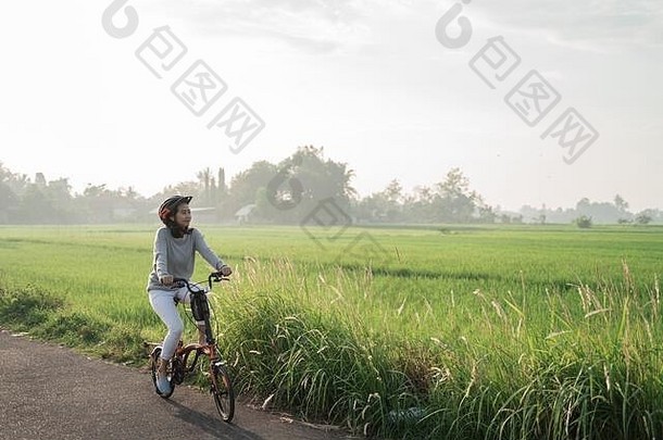 亚洲妇女戴着头盔在稻田里骑<strong>折叠自行车</strong>