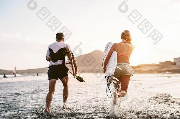 快乐冲浪者运行水日落时间年轻的夫妇有趣的冲浪海洋极端的体育运动青年文化生活方式概念