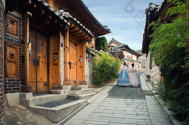两名穿着韩服的妇女在韩国首尔的布克雄汉诺村的传统风格房屋中行走。