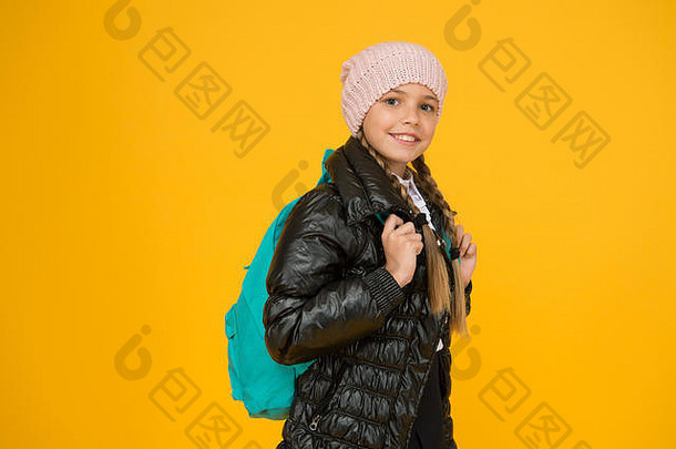 可爱的学生。时尚概念。女孩戴针织帽子，穿黄色背景的夹克。为上学季节买衣服。女学生时装。秋冬。背着背包的孩子。时装店。