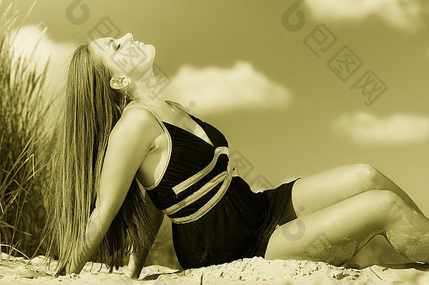 暑假一天的自由时间概念。坐在海滩上享受日光浴的女人。