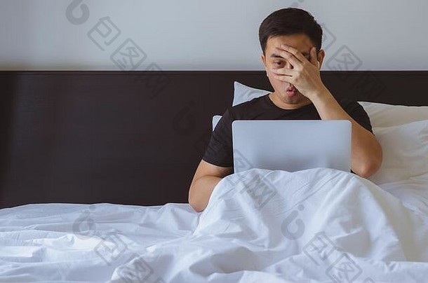亚洲男子在床上的笔记本电脑前观看恶心的视频剪辑。冠状病毒C2019冠状病毒疾病的家内隔离与隔离