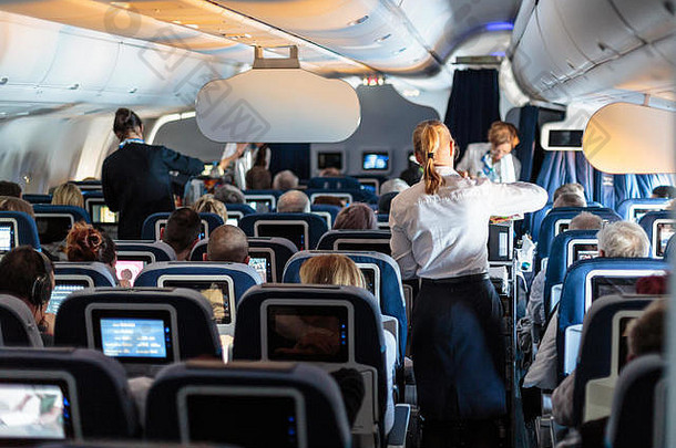 大型商用飞机的内部，飞行中有空姐在座位上为乘客服务。