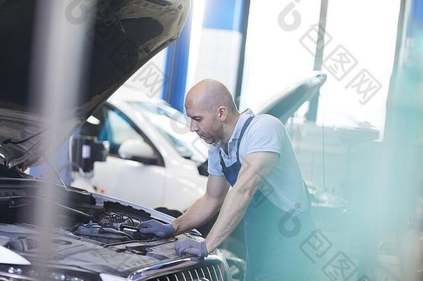 在车库、复印区进行检查时，肌肉发达的汽车修理工观察打开的汽车引擎盖的侧视图