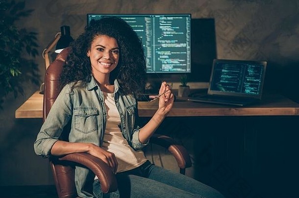 肖像积极的熟练的非洲式发型美国女孩网络设计师工程师坐椅子享受晚上公司数据工作持有眼镜工作场所