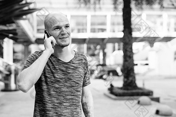 年轻快乐的秃头男人在商场外用手机思考和交谈