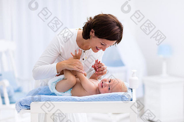 年轻的妈妈。采取护理男孩白色阳光明媚的托儿所改变表格婴儿婴儿床摇摆椅子