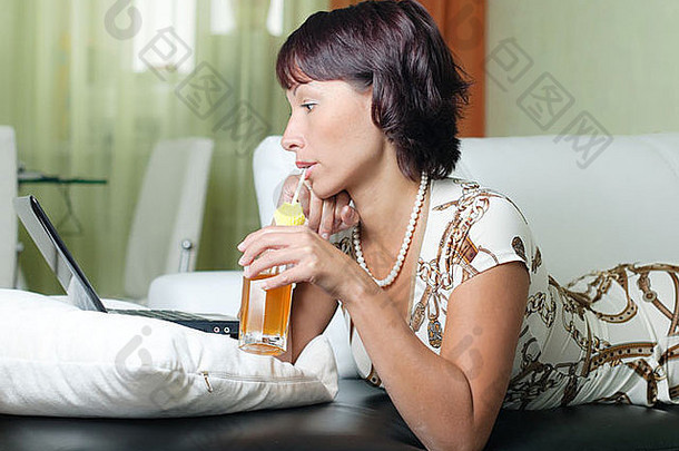 一位年轻女子躺在沙发上，写着笔记本，喝着果汁