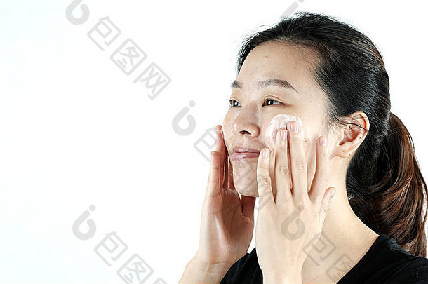 可爱的亚洲女孩在脸上涂抹乳霜乳液，隔离在白色背景上