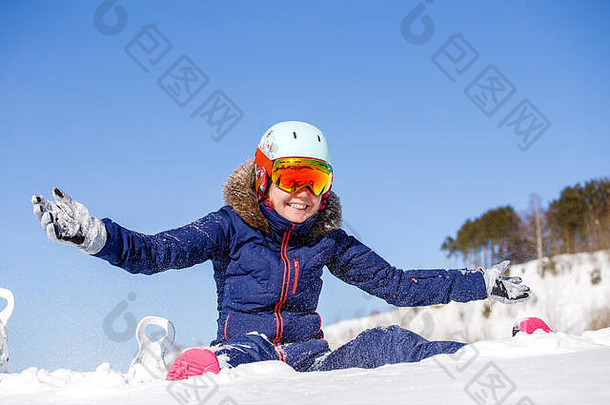 女运动员戴头盔坐在雪堆旁的照片