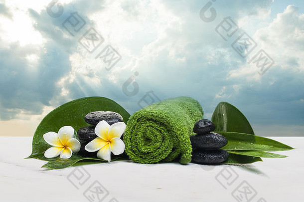 用毛巾和鲜花进行热带健康治疗的水疗用品。水疗健康理念，云层、天空和阳光。