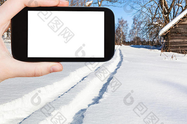 旅游理念——在俄罗斯斯摩棱斯克地区阳光明媚的冬日，游客在智能手机上拍摄滑雪道通往森林的照片