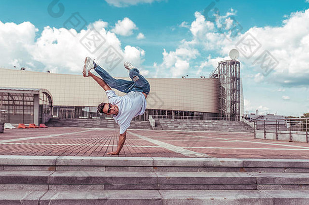 年轻活跃的舞蹈家是单臂站在跳跃，一个运动人，城市夏季，霹雳舞，嘻哈运动，现代舞，青年生活方式。大街