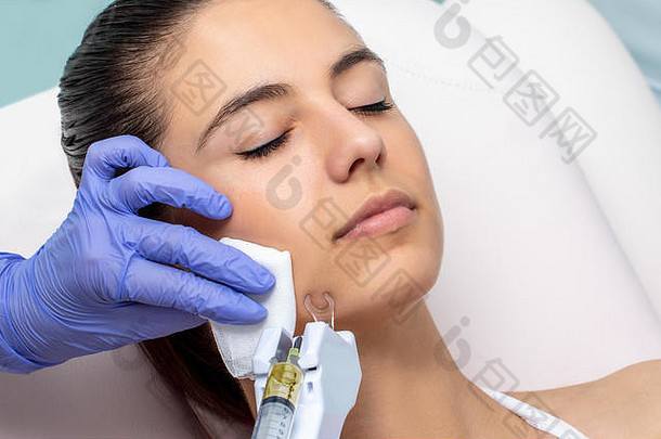 治疗师正在对年轻女子进行彗星式面部等离子提升术。手戴乳胶手套，在下巴上应用微针技术。