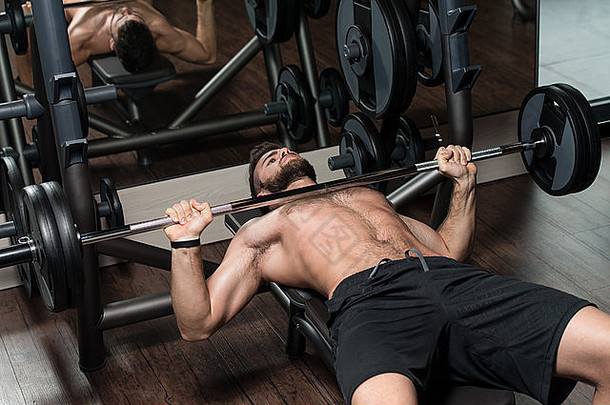 一个帅哥正在一家现代化的健身房里用杠铃锻炼<strong>胸</strong>部