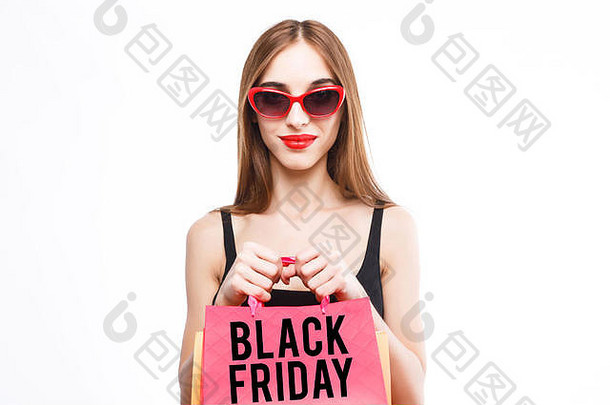 可爱的快乐浅黑肤色的女人女人穿黑色的衣服太阳镜持有粉红色的购物袋前面白色背景概念消费主义出售丰富的生活