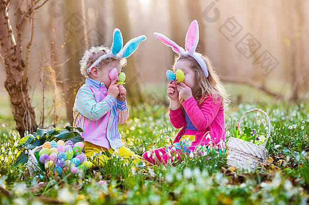 孩子们在盛开的春天花园里寻找复活节彩蛋。有<strong>兔</strong>子耳朵的孩子们在雪花中寻找五颜六色的蛋